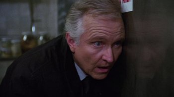 Movie still from “Re-Animator” (1985), directed by Stuart Gordon – An older man in a black shirt and a tie; Close Up shot, Low angle