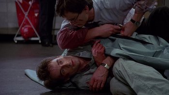 Movie still from “Re-Animator” (1985), directed by Stuart Gordon – A man is lying on the ground while another man is standing over him; Close Up shot, Over the shoulder angle
