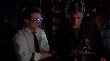 Movie still from “Re-Animator” (1985), directed by Stuart Gordon – Two men sitting in a dark room looking at a cell phone; Medium shot, Low angle