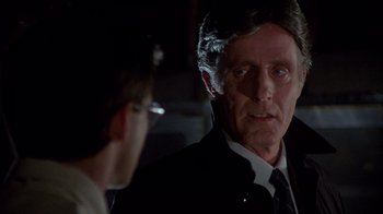 Movie still from “Re-Animator” (1985), directed by Stuart Gordon – A man wearing a suit and tie talking to another man; Close Up shot, Over the shoulder angle