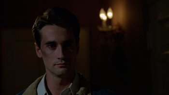 Movie still from “Re-Animator” (1985), directed by Stuart Gordon – A young man is standing in a dark room; Close Up shot, Over the shoulder angle