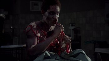 Movie still from “Re-Animator” (1985), directed by Stuart Gordon – A man with blood on his face is holding a red object; Medium shot, Low angle