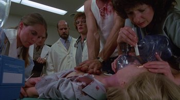 Movie still from “Re-Animator” (1985), directed by Stuart Gordon – A group of people standing around a woman with blood on her face; Medium shot, Low angle