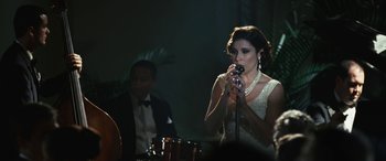 Movie still from “Reaching for the Moon” (2013), directed by Bruno Barreto – A woman in a white dress holding a microphone; Medium shot, Over the shoulder angle