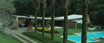 Movie still from “Reaching for the Moon” (2013), directed by Bruno Barreto – A group of people sitting in a yard next to a pool; Extreme Wide shot, High angle