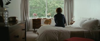 Movie still from “Reaching for the Moon” (2013), directed by Bruno Barreto – A woman sitting on a bed looking out a window; Wide shot, High angle