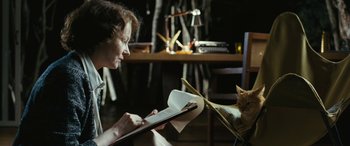 Movie still from “Reaching for the Moon” (2013), directed by Bruno Barreto – A woman is reading a book to a cat; Medium shot, Over the shoulder angle