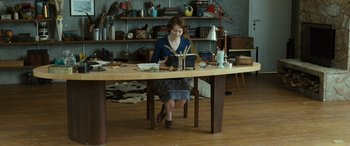 Movie still from “Reaching for the Moon” (2013), directed by Bruno Barreto – A woman sitting at a table in a room; Wide shot, High angle