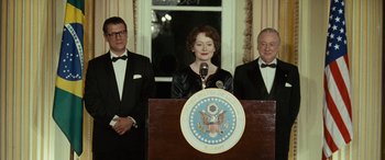 Movie still from “Reaching for the Moon” (2013), directed by Bruno Barreto – A woman standing at a podium in front of two other men; Medium shot, Low angle