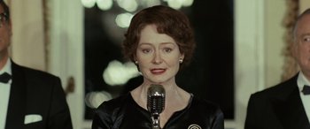 Movie still from “Reaching for the Moon” (2013), directed by Bruno Barreto – A woman in a black shirt is holding a microphone; Close Up shot, Over the shoulder angle