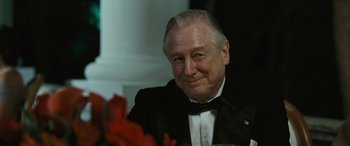 Movie still from “Reaching for the Moon” (2013), directed by Bruno Barreto – An older man in a tuxedo sitting in front of flowers; Close Up shot, Over the shoulder angle
