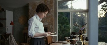 Movie still from “Reaching for the Moon” (2013), directed by Bruno Barreto – A woman standing at a table holding papers in her hands; Medium shot, Over the shoulder angle