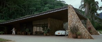 Movie still from “Reaching for the Moon” (2013), directed by Bruno Barreto – A car is parked in front of a stone building; Wide shot, Low angle