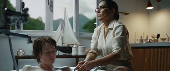 Movie still from “Reaching for the Moon” (2013), directed by Bruno Barreto – A woman sitting in front of a window with a sailboat in the background; Medium shot, Over the shoulder angle