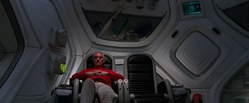 Movie still from “Red Planet” (2000), directed by Antony Hoffman – A man sitting in an airplane seat in the middle of the day; Medium shot, Overhead angle