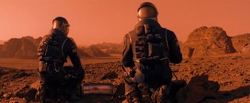 Movie still from “Red Planet” (2000), directed by Antony Hoffman – A man in a space suit is looking at a tv screen; Wide shot, Over the shoulder angle