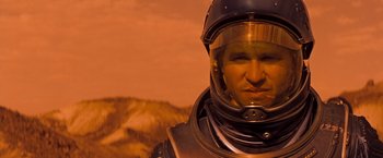 Movie still from “Red Planet” (2000), directed by Antony Hoffman – A man in a space suit is standing in front of a mountain; Close Up shot, Low angle