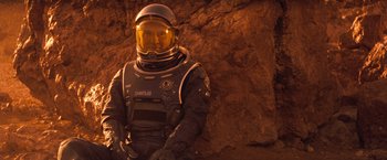 Movie still from “Red Planet” (2000), directed by Antony Hoffman – A man in a spacesuit standing in front of a rock wall; Medium shot, High angle