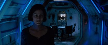 Movie still from “Red Planet” (2000), directed by Antony Hoffman – A woman standing in a room with a table and chairs in front of it; Medium shot, Low angle