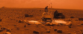 Movie still from “Red Planet” (2000), directed by Antony Hoffman – A group of people sitting on top of a dirt field; Extreme Wide shot, High angle