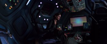 Movie still from “Red Planet” (2000), directed by Antony Hoffman – A woman sitting on a chair in a room with lights on; Wide shot, High angle