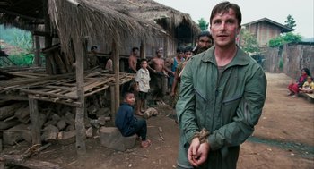 Movie still from “Rescue Dawn” (2006), directed by Werner Herzog – A group of people standing in front of a hut; Medium shot, Over the shoulder angle