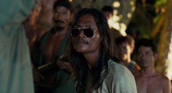 Movie still from “Rescue Dawn” (2006), directed by Werner Herzog – A man with long black hair wearing sunglasses; Close Up shot, Over the shoulder angle