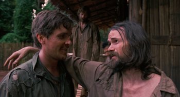 Movie still from “Rescue Dawn” (2006), directed by Werner Herzog – A man with long hair and a long beard standing next to another man with long hair; Medium shot, Over the shoulder angle