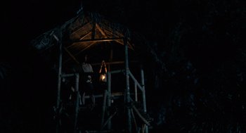 Movie still from “Rescue Dawn” (2006), directed by Werner Herzog – Two people sitting in a wooden hut at night; Extreme Wide shot, Low angle