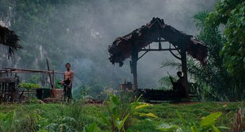 Movie still from “Rescue Dawn” (2006), directed by Werner Herzog – A man standing next to a wooden gazebo in the middle of a forest; Extreme Wide shot, Low angle
