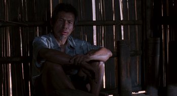 Movie still from “Rescue Dawn” (2006), directed by Werner Herzog – A man sitting on a chair in front of a wooden fence; Medium shot, Low angle