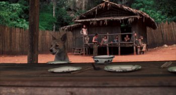 Movie still from “Rescue Dawn” (2006), directed by Werner Herzog – A dog sitting in front of a bowl on a wooden table; Wide shot, Over the shoulder angle