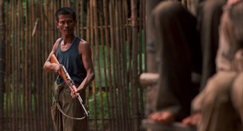 Movie still from “Rescue Dawn” (2006), directed by Werner Herzog – A man holding a flute in front of a person; Medium shot, Over the shoulder angle