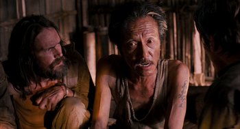 Movie still from “Rescue Dawn” (2006), directed by Werner Herzog – An older man with tattoos and a beard; Close Up shot, Over the shoulder angle