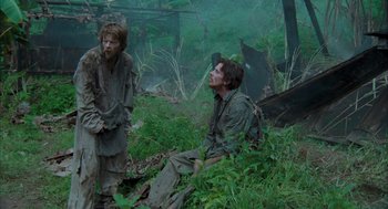 Movie still from “Rescue Dawn” (2006), directed by Werner Herzog – Two men are sitting in the grass near a forest; Wide shot, Low angle