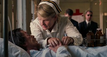 Movie still from “Rescue Dawn” (2006), directed by Werner Herzog – A woman in a nurse's uniform is tending to a man; Medium shot, Over the shoulder angle