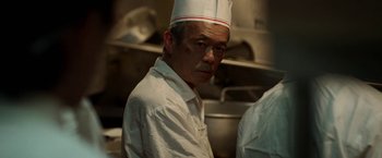 Movie still from “Revenge of the Green Dragons” (2014), directed by Andrew Loo – A man wearing a chef's hat in a kitchen; Close Up shot, Low angle