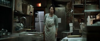 Movie still from “Revenge of the Green Dragons” (2014), directed by Andrew Loo – A woman standing in a kitchen wearing an apron; Medium shot, High angle