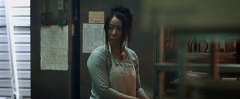 Movie still from “Revenge of the Green Dragons” (2014), directed by Andrew Loo – A woman wearing an apron standing next to a wall; Medium shot, Low angle