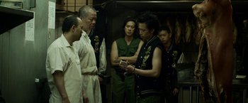 Movie still from “Revenge of the Green Dragons” (2014), directed by Andrew Loo – A group of men standing around each other in a room; Medium shot, Over the shoulder angle