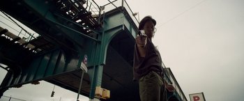 Movie still from “Revenge of the Green Dragons” (2014), directed by Andrew Loo – A man holding a gun in front of a bridge; Medium shot, Low angle