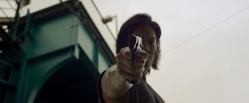 Movie still from “Revenge of the Green Dragons” (2014), directed by Andrew Loo – A person holding a gun in their hand; Close Up shot, Low angle