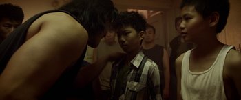 Movie still from “Revenge of the Green Dragons” (2014), directed by Andrew Loo – A group of young men standing around a young boy; Medium shot, Over the shoulder angle