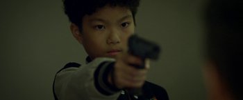 Movie still from “Revenge of the Green Dragons” (2014), directed by Andrew Loo – A young boy is holding a gun in his hand; Close Up shot, High angle