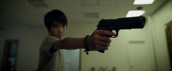 Movie still from “Revenge of the Green Dragons” (2014), directed by Andrew Loo – A young boy is holding a gun in a room; Close Up shot, Low angle