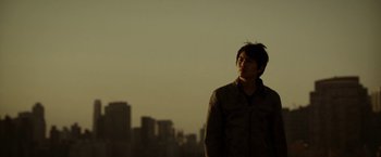 Movie still from “Revenge of the Green Dragons” (2014), directed by Andrew Loo – A man standing in front of a city skyline at dusk; Close Up shot, Low angle