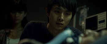 Movie still from “Revenge of the Green Dragons” (2014), directed by Andrew Loo – A young man looking at the camera while holding a microphone; Close Up shot, High angle