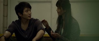 Movie still from “Revenge of the Green Dragons” (2014), directed by Andrew Loo – A man and a woman sitting on a couch talking to each other; Medium shot, Over the shoulder angle