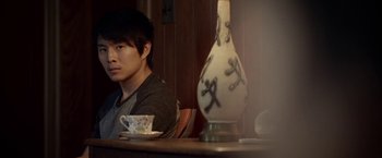 Movie still from “Revenge of the Green Dragons” (2014), directed by Andrew Loo – A man sitting at a table with a cup of coffee; Close Up shot, Over the shoulder angle