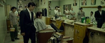 Movie still from “Revenge of the Green Dragons” (2014), directed by Andrew Loo – A group of men sitting in a barber shop; Wide shot, Over the shoulder angle